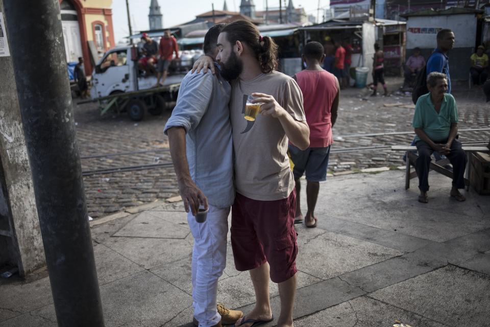 In this Sept. 7, 2019 photo, drunk men embrace early in the morning at the Ver-o-Peso riverside market in Belém, Brazil. Their night probably fueled by plenty of Brazil’s cachaca sugarcane liquor - with some bottles filled with jambú, the Amazonian herb that sparks a tingling, electric shock-like sensation to the tongue. (AP Photo/Rodrigo Abd)