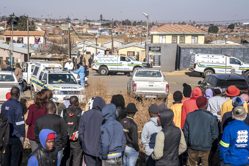 People gather at the scene of an overnight bar shooting in Soweto, South Africa, Sunday July 10, 2022. A mass shooting at a tavern in Johannesburg's Soweto township has killed 15 people and left others in critical condition, according to police. Police say they are investigating reports that a group of men arrived in a minibus taxi and opened fire on some of the patrons at the bar shortly after midnight Sunday. (AP Photo/Shiraaz Mohamed)