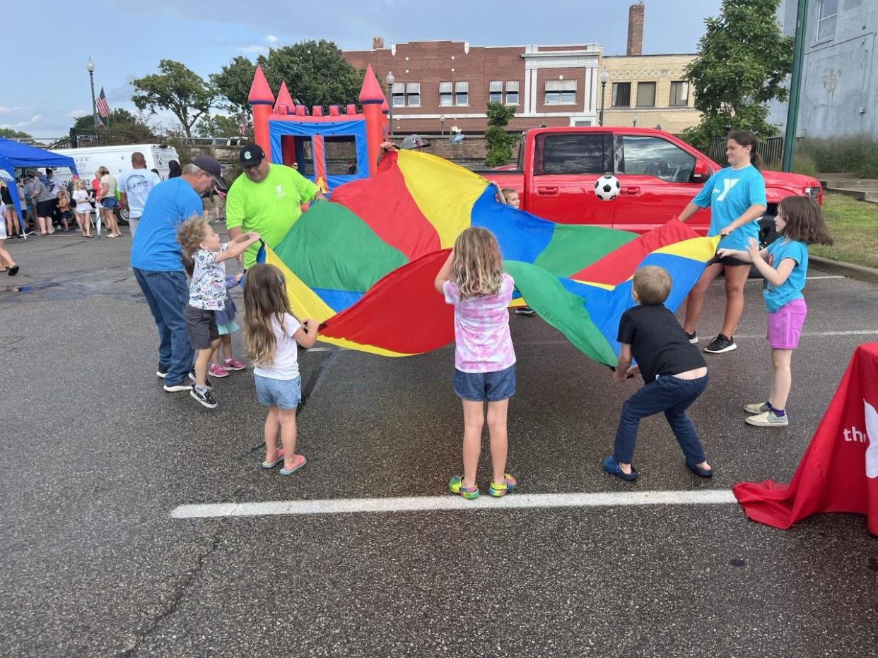 Children and Monroe Family YMCA staff play with a big parachute at a previous Y on the Fly stop.