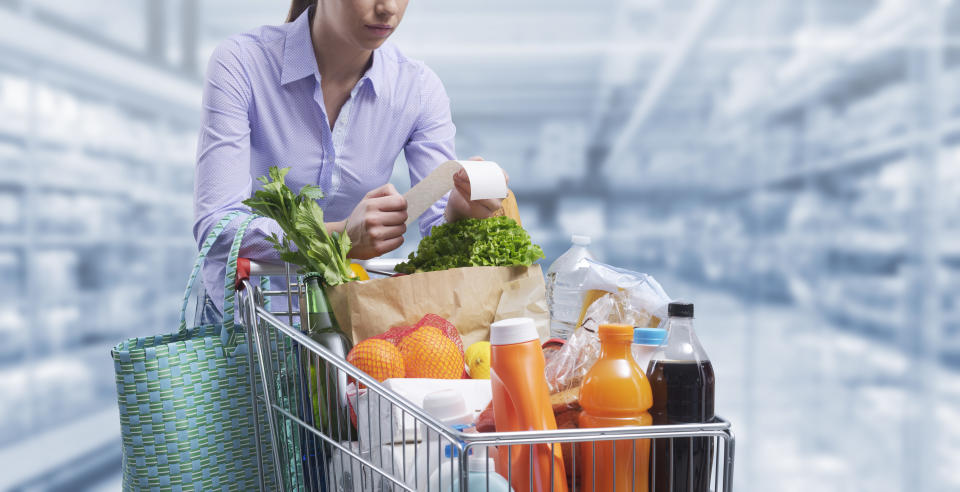 Woman pushing cart and checking grocery receipt, grocery shopping, expenses concept