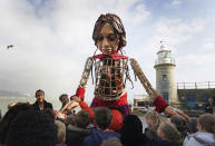 Little Amal, a 3.5-metre-tall puppet of a nine-year-old Syrian girl, is greeted by children from the St. Mary's Primary Academy as she arrives in Folkestone, Kent, Tuesday, Oct. 19, 2021 as part of the Handspring Puppet Company's 'The Walk'. The puppet started her journey in Turkey on 27 July and has travelled nearly 8,000 km across Greece, Italy, Germany, Switzerland, Belgium and France, symbolizing millions of displaced children. (Gareth Fuller/PA via AP)