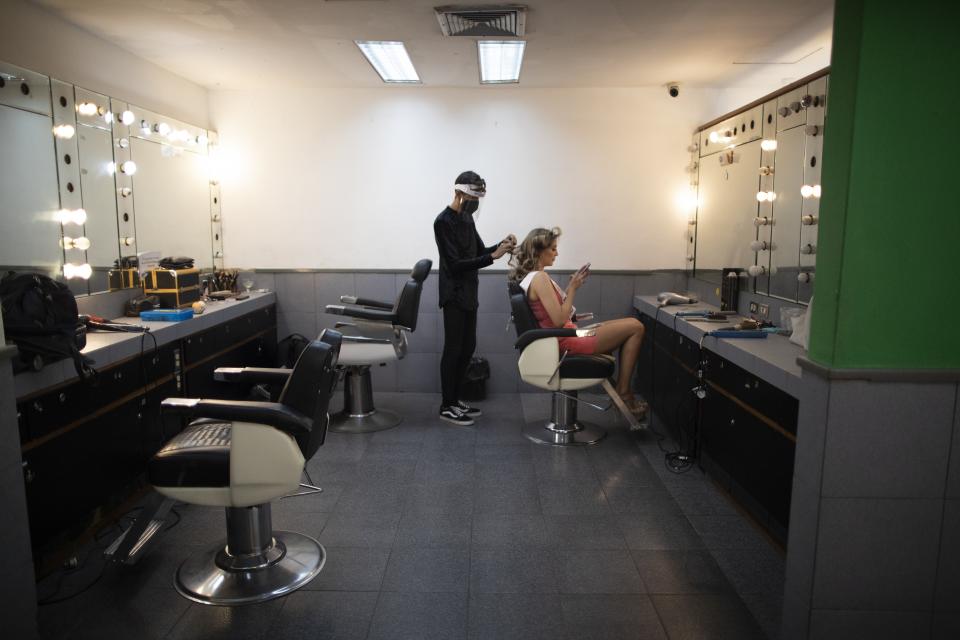 Distrito Capital state beauty pageant contestant Elizabeth Gasiba, wearing a protective face mask, passes the time on her phone as her hair is styled, in a Venevision television station dressing room in Caracas, Venezuela, Friday, Sept. 18, 2020. Quarantine rules and social distancing has forced the contestants to train at home and online with limited access to the venue itself where strict measures are in place. The Miss Venezuela pageant is due to take place on Sept. 24. (AP Photo/Ariana Cubillos)