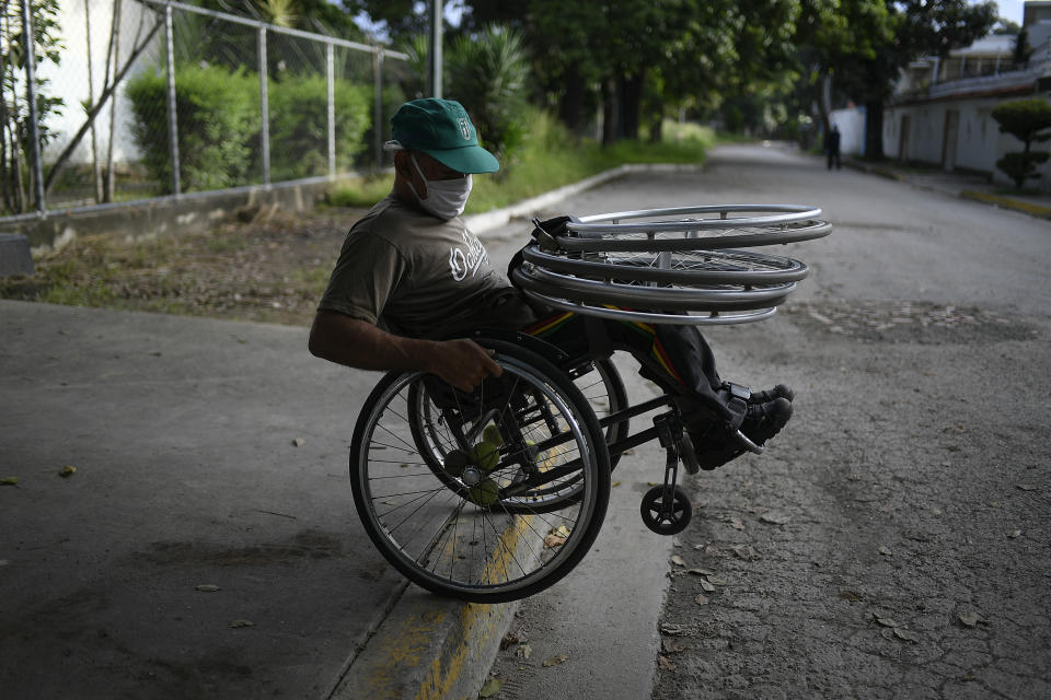 Manuel Mendoza rueda por una acera para inflar neumáticos para sillas de ruedas en un taller de automóviles en el barrio La Paz de Caracas, Venezuela, el sábado 21 de noviembre de 2020. (AP Foto/Matias Delacroix)