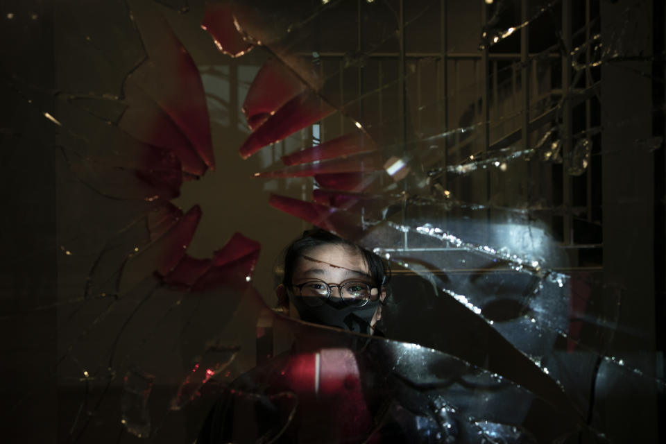 In this Oct. 16, 2019, photo, a 14-year-old protester who identified herself as K.C., poses for a portrait as a projector displays a photograph, previously taken during the unrest, over her at a protest in Hong Kong. For many protesters, identity is entwined with surveillance. Their signature masks, umbrellas and top-to-bottom black outfits shield them not only from physical threats like the riot police's tear gas and rubber bullets, but also from the invisible dangers of government identification and tracking. (AP Photo/Felipe Dana)