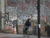 A cyclist wears a mask as he passes graffitti in London, Saturday, Jan. 23, 2021 during England's third national lockdown since the coronavirus outbreak began. The U.K. is under an indefinite national lockdown to curb the spread of the new variant, with nonessential shops, gyms and hairdressers closed, and people being told to stay at home. (AP Photo/Kirsty Wigglesworth)