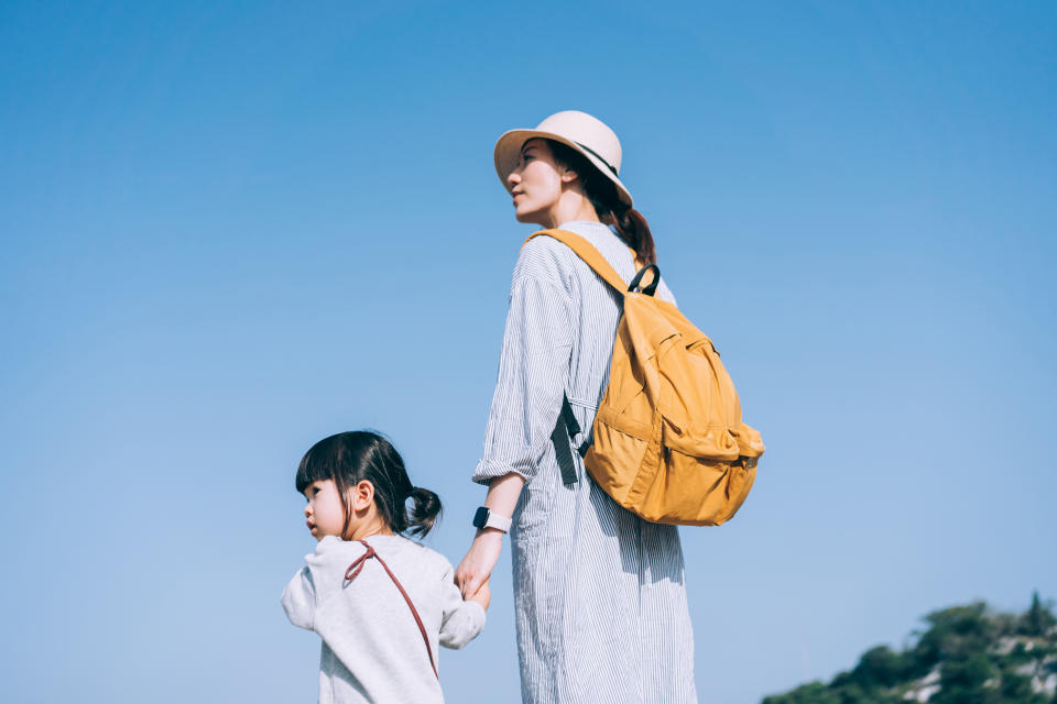 Young Asian mother holding hands of daughter hiking and enjoying weekend in the nature. Looking up to the sky while standing against blue sky. They are spending some quality bonding time together, enjoying the nature and beautiful scenics on a sunny day