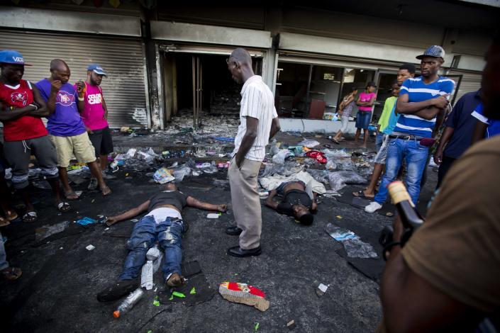<p>The bodies of two men lie outside a burned and looted store, as one of the men’s relatives stands between them, after two days of protests against a planned hike in fuel prices in Port-au-Prince, Haiti, Sunday, July 8, 2018. (Photo: Dieu Nalio Chery/AP) </p>