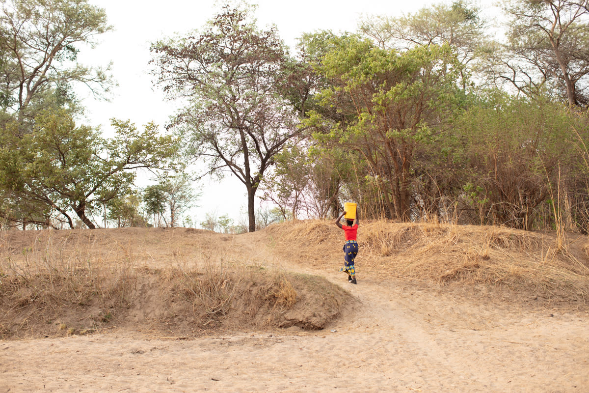 A woman from the Mukobela community in Zambia carries water near a dried-up riverbed (WaterAid/Laura Pannack/PA)