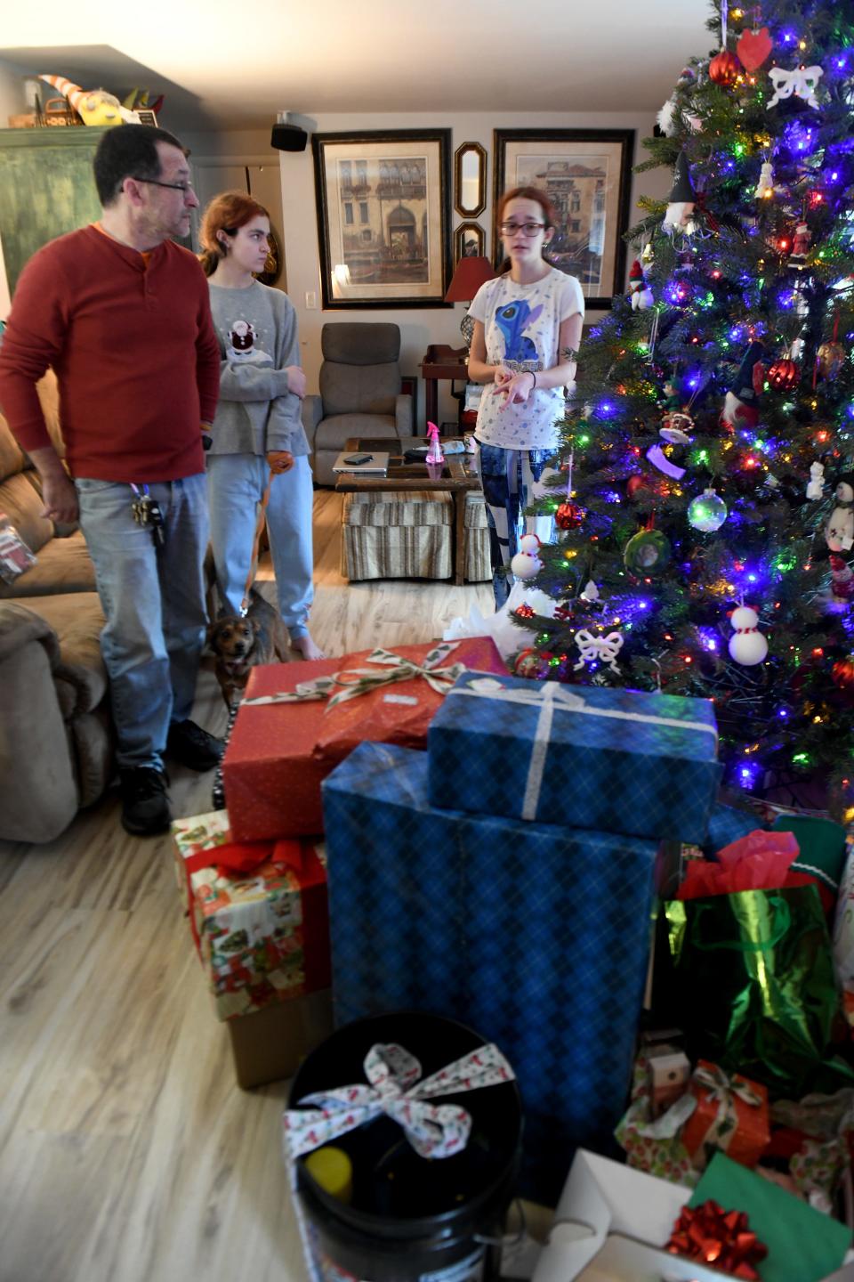 Michael Buzzelli of Alliance stands Saturday, Dec. 23, 2023, with daughters Grace and Nancy and admires gifts in his living room after the delivery of a car from Sally & Assoc. Auto Sales, Inc., in Alliance. The dealership's giveaway is in its 18th year.