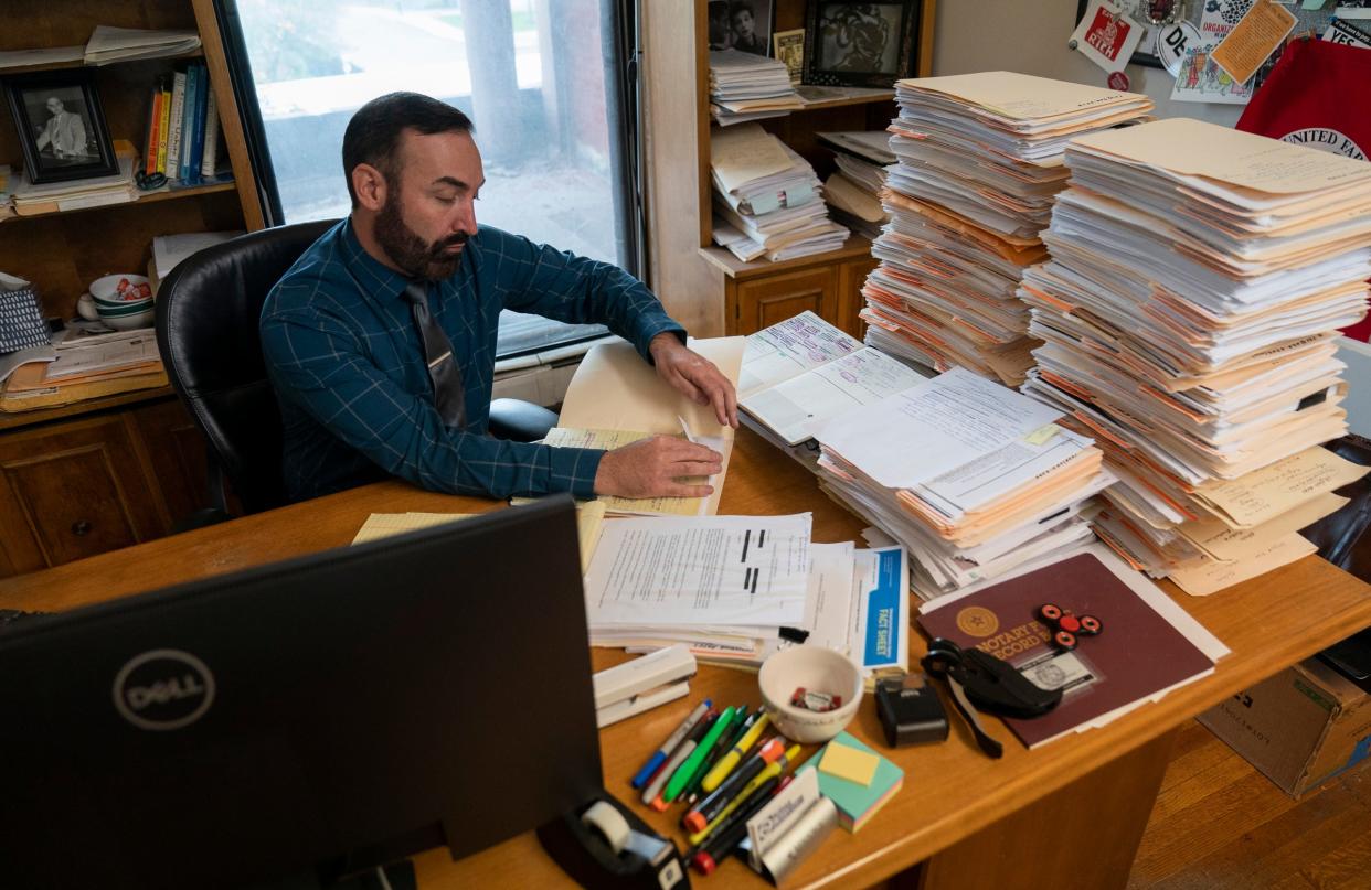 Tony Paris, an attorney with the Sugar Law Center for Economic and Social Justice in Detroit, works at his desk with two large piles of clients open cases that deal with unemployment claims on Thursday, Oct. 26, 2023.
