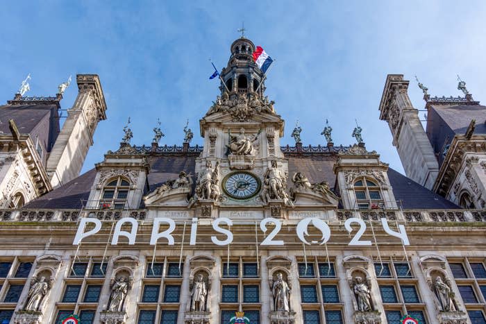 Paris city hall with "Paris 2024" banners, promoting the 2024 Summer Olympics, the French flag on top, and statues along the building facade