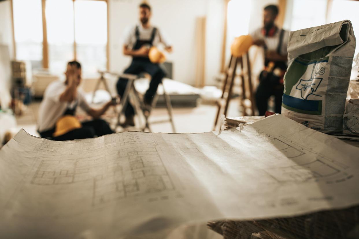 close up of blueprints at construction site with manual workers in the background