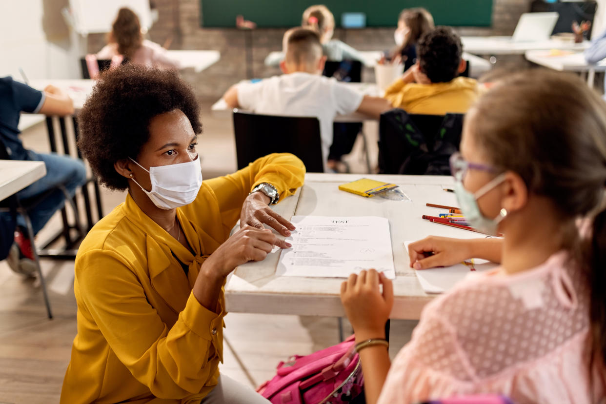 A teacher and a student in a classroom wearing protective face masks discuss test results. 