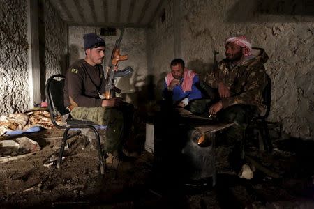 Rebel fighters of the Al-Furqan brigade keep warm by a fire with their weapons in Aziziyah village, southern Aleppo countryside, Syria March 5, 2016. REUTERS/Khalil Ashawi