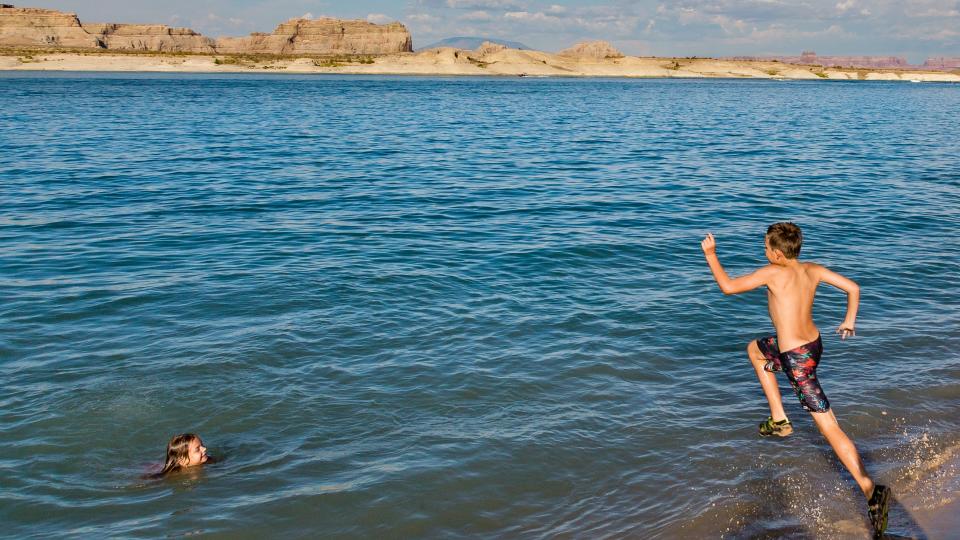 A boy runs to jump in the lake while a girl in the water watches