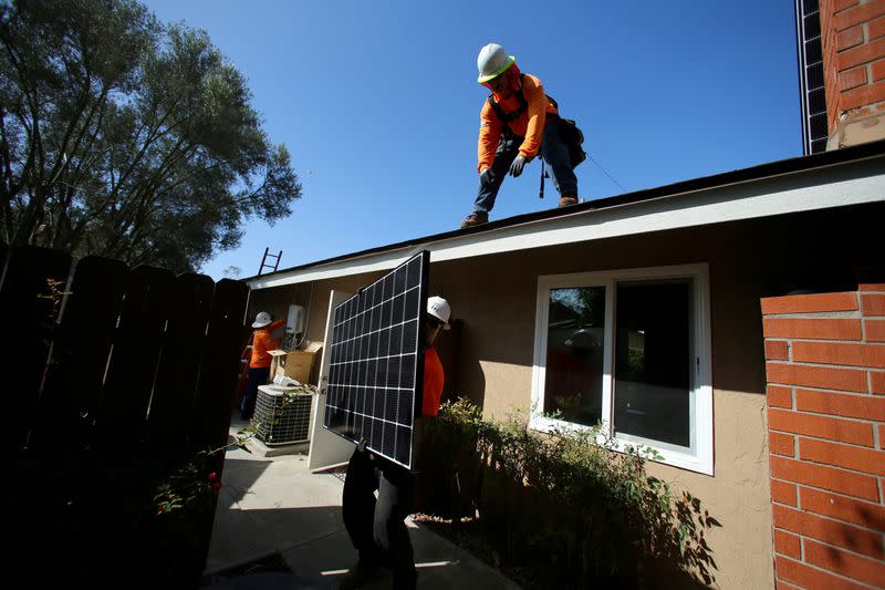 FILE PHOTO: Workers lift a solar panel onto a roof during a residential solar installation in Scripps Ranch, San Diego, California