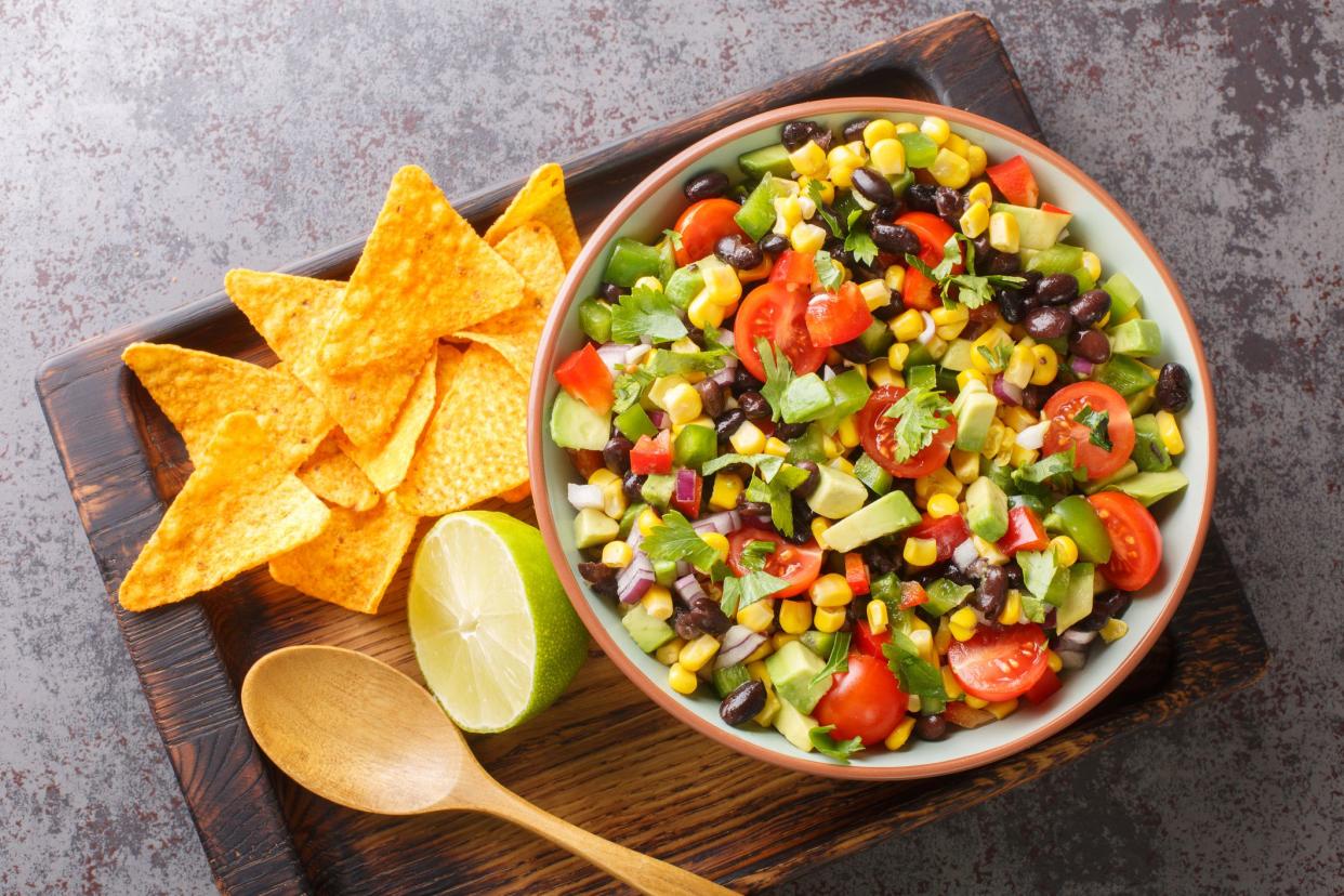 Homemade Cowboy salad or Texas caviar bean dip lime dressing, served with tortilla chips closeup in the bowl on the wooden board. Horizontal top view from above