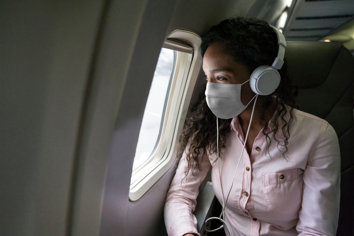 Woman listening to music while flying on an airplane wearing a facemask