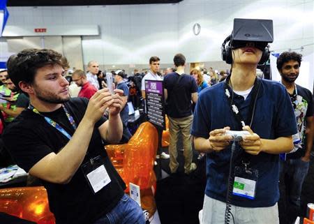 Software designer Julian Kantor (L), who created "The Recital" takes a picture of Jonathan Feng (R) as he uses the Oculus Rift virtual reality headset to experience his program during E3 in Los Angeles, California June 12, 2013. REUTERS/Gus Ruelas