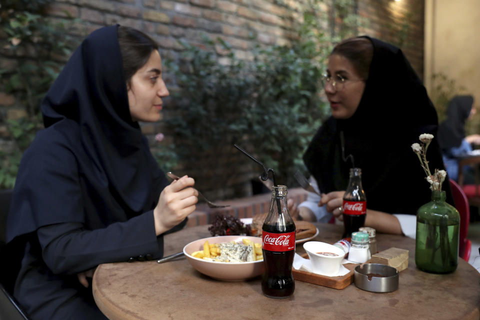 Two Iranians enjoy their time while two Coca-Cola stand on their table at a cafe in downtown Tehran, Iran, Wednesday, July 10, 2019. Whether at upscale restaurants or corner stores, American brands like Coca-Cola and Pepsi can be seen throughout Iran despite the heightened tensions between the two countries. U.S. sanctions have taken a heavy toll, but Western food, movies, music and clothing are still widely available. (AP Photo/Ebrahim Noroozi)
