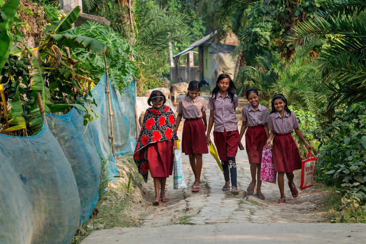Five young girls in a uniform of red skirts and pink shirts walk home from school.