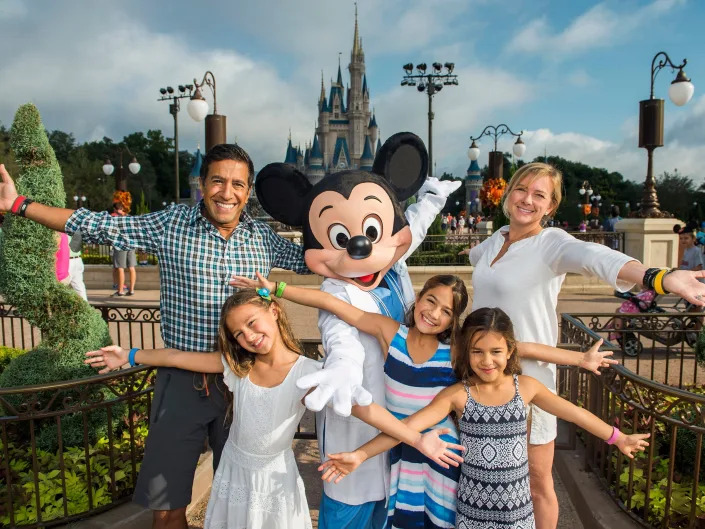 Photo of two parents and three daughters with their arms open with Mickey Mouse.