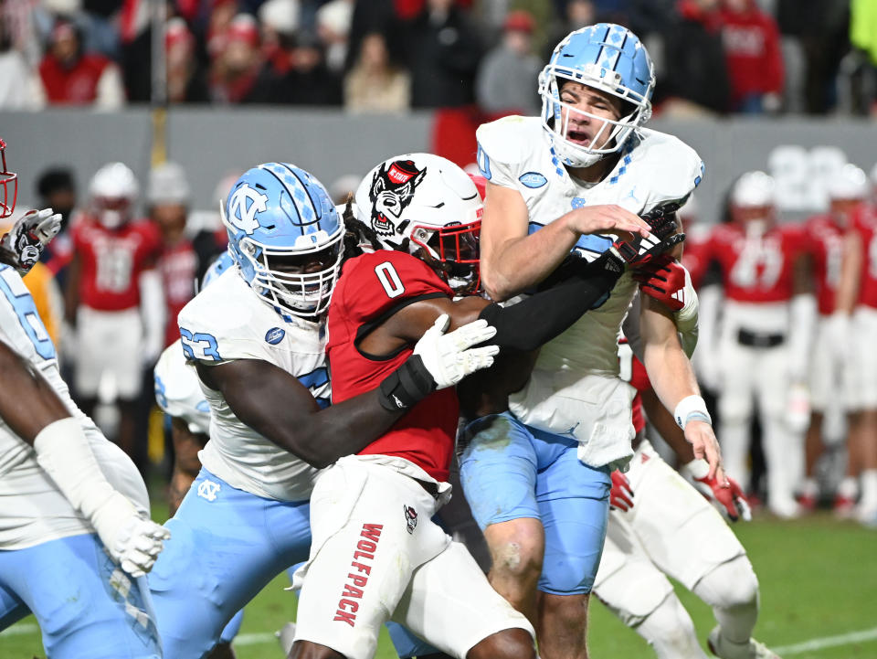 Nov 25, 2023; Raleigh, North Carolina, USA; North Carolina Tar Heels quarterback Drake Maye (10) is hit after throwing a pass by North Carolina State Wolfpack safety Sean Brown (0) during the first half at Carter-Finley Stadium. Mandatory Credit: Rob Kinnan-USA TODAY Sports