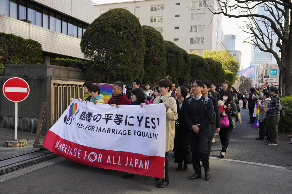 Plaintiffs holding a banner walk into the Tokyo district court for the ruling regarding LGBTQ+ marriage rights as supporters, right, of the LGBTQ+ community wave rainbow flags in Tokyo, Thursday, March 14, 2024. The Japanese court on Thursday ruled that not allowing same-sex couples the same marital benefits as heterosexuals violates their fundamental right to have a family, but the current civil law did not take into consideration sexual diversity and is not clearly unconstitutional, a partial victory for Japan's LGBTQ+ community calling for equal marriage rights. (AP Photo/Hiro Komae)