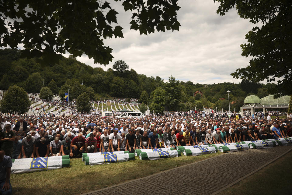 Bosnian muslim men pray next to the coffins containing the remains of 50 newly identified victims of Srebrenica Genocide in Potocari, Monday, July 11, 2022. Thousands converge on the eastern Bosnian town of Srebrenica to commemorate the 27th anniversary on Monday of Europe's only acknowledged genocide since World War II. (AP Photo/Armin Durgut)