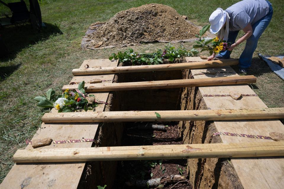 Diana McDowell places flower arrangements around the grave in preparation for the first green burial at the Windy Knoll Memorial Sanctuary in Lawrenceburg -- the first green cemetery in the state of Kentucky. A green burial means the body within the casket is not embalmed, and the casket is either made of wood or is simply a linen shroud. There are no large headstones. July 14, 2023