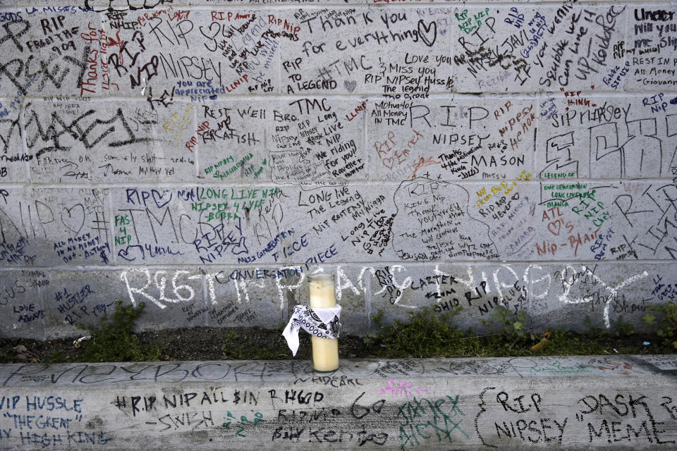 FILE - This April 11, 2019 file photo shows a lone candle against a wall full of messages commemorating slain rapper Nipsey Hussle outside The Marathon Clothing store in Los Angeles. Hussle, 33, was shot and killed outside his clothing store on March 31, 2019. A year after his death, his popularity and influence are as strong as ever. He won two posthumous Grammys in January, he remains a favorite of his hip-hop peers and his death has reshaped his hometown of Los Angeles in some unexpected ways. (AP Photo/Jae C. Hong, File)