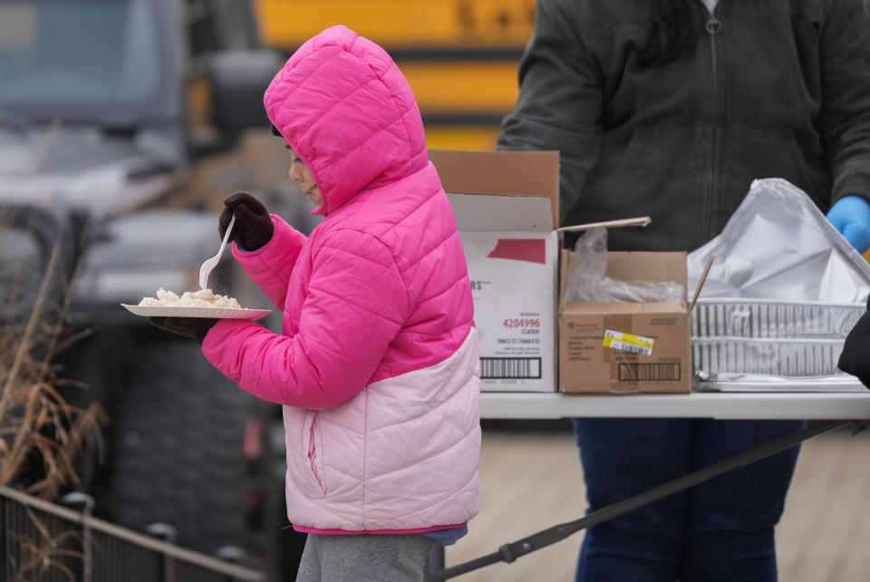 A young migrant receives food from the nonprofit Chi-Care Thursday, Jan. 11, 2024, in Chicago. In the city of Chicago's latest attempt to provide shelter to incoming migrants, several CTA buses were parked in the area of 800 South Desplaines Street to house people in cold winter weather. (AP Photo/Erin Hooley)