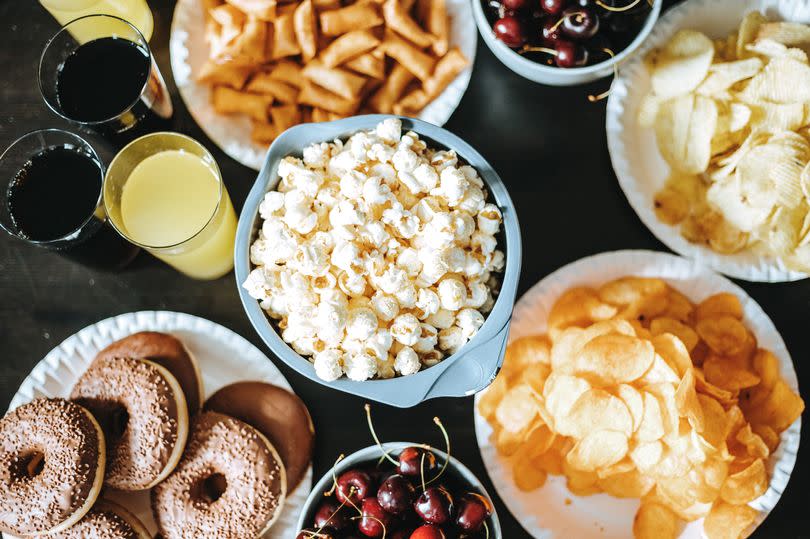 Directly above photo of dark table with various bowls of different snacks and desserts and glasses of drink ready to consume at dinner party