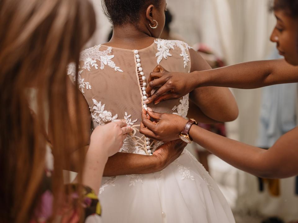 Woman trying on wedding dress with female friends having fun and helping her fit the dress - stock photo