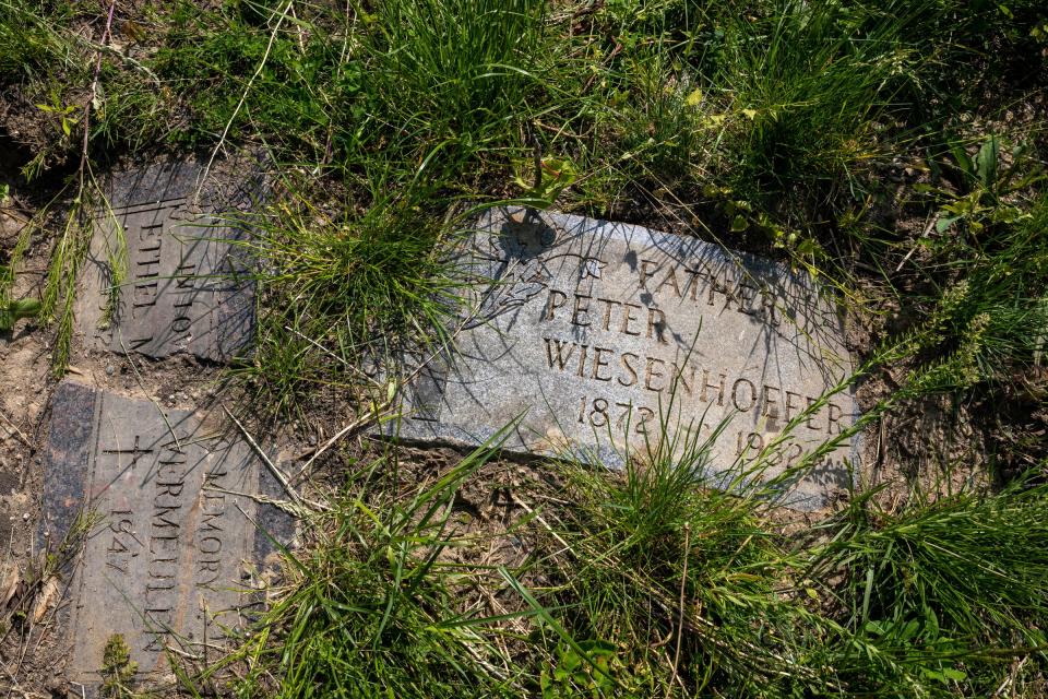 A headstone with the name Peter Wiesenhoefer sits surrounded in weeds and grass next to a few other headstones on an empty lot in Doyle Street off of Van Dyke in Detroit on Thursday, May 16, 2024.