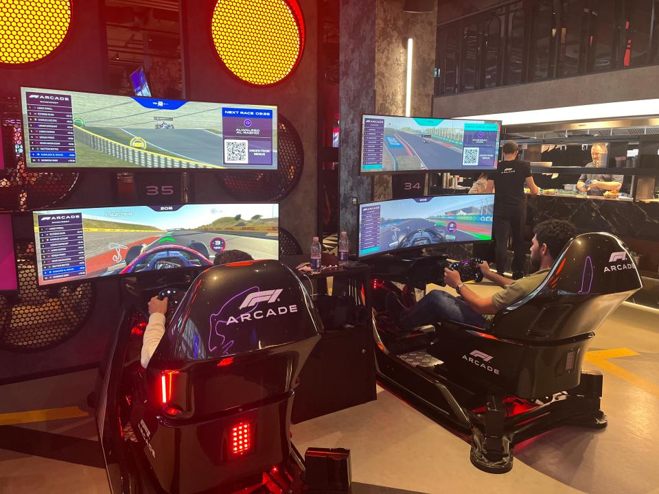Two men drive on the racing simulators at the F1 Arcade.