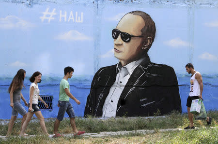 People walk past a graffiti depicting Russian President Vladimir Putin seen on a residential building in Simferopol, Crimea, August 19, 2015. The sign on the graffiti reads, "Ours". REUTERS/Pavel Rebrov/File Photo