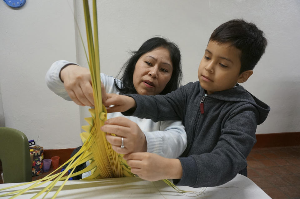 Maria Consuelo Palapa weaves a palm frond in a traditional Mexican design with help from her son Omar, 7, at the Church of the Incarnation in Minneapolis on Wednesday, March 29, 2023. The parishioner at this Catholic church, where the palms will be sold as a fundraiser and blessed at Palm Sunday services this weekend, said she joined the volunteer workshop “to first help the church, and to teach the child my traditions.” (AP Photo/Giovanna Dell’Orto)