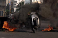 A man rides his scooter through the smoke of burning tires, that were set on fire by protesters to block a road, in Beirut, Lebanon, Thursday, March 4, 2021. Lebanon has been hit by one crisis after another, with widespread protests against the country’s corrupt political class breaking out in October 2019. (AP Photo/Bilal Hussein)