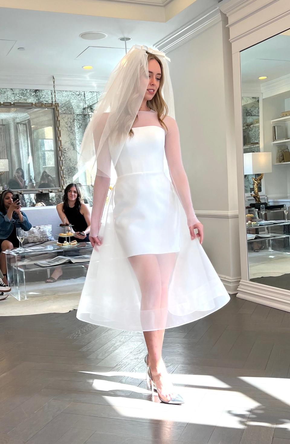 A woman poses in a mini wedding dress with a sheer over skirt.