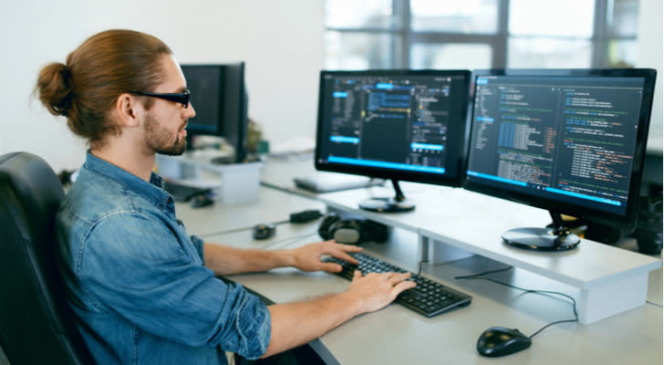 professional with manbun working on software on two monitors at a desk