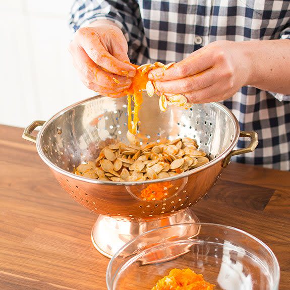 Person separating pumpkin seeds from orange gunk in a metal bowl