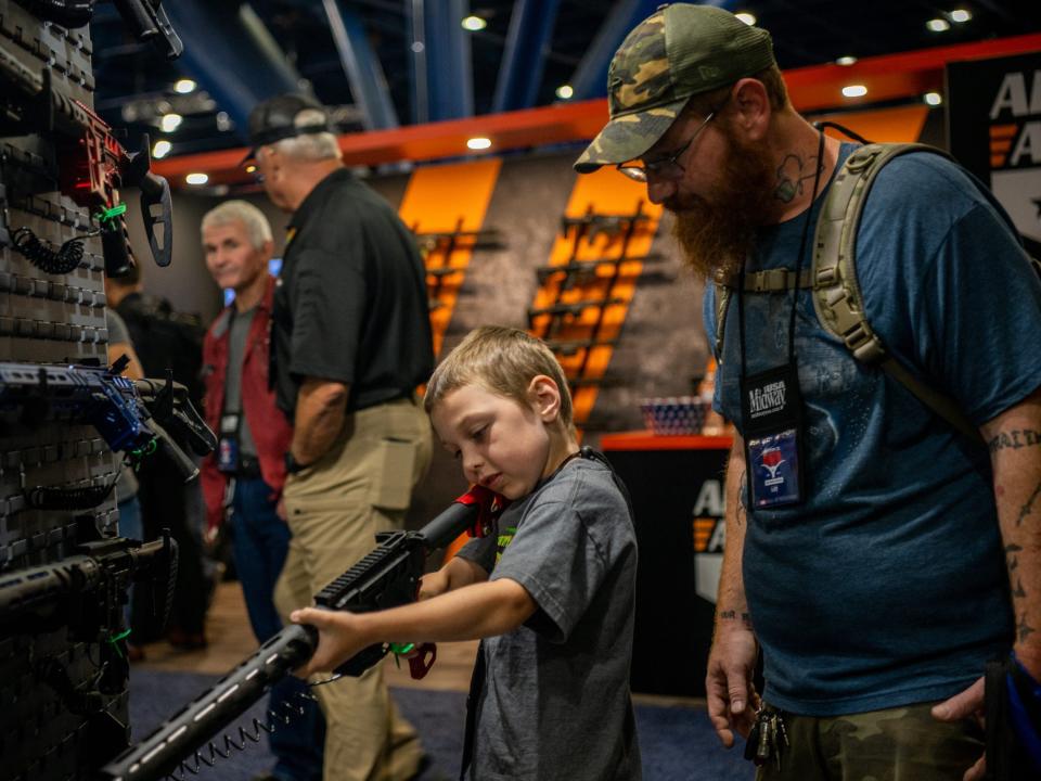 A man and his 7-year-old son look at an AR-15-style rifle at an NRA convention in 2022.