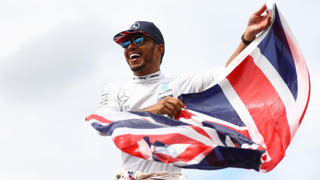  Mercedes driver Lewis Hamilton stands on top of the pitlane fence waving a Union Jack flag to celebrate his win with the British fans ay the F1 British Grand Prix at Silverstone.  