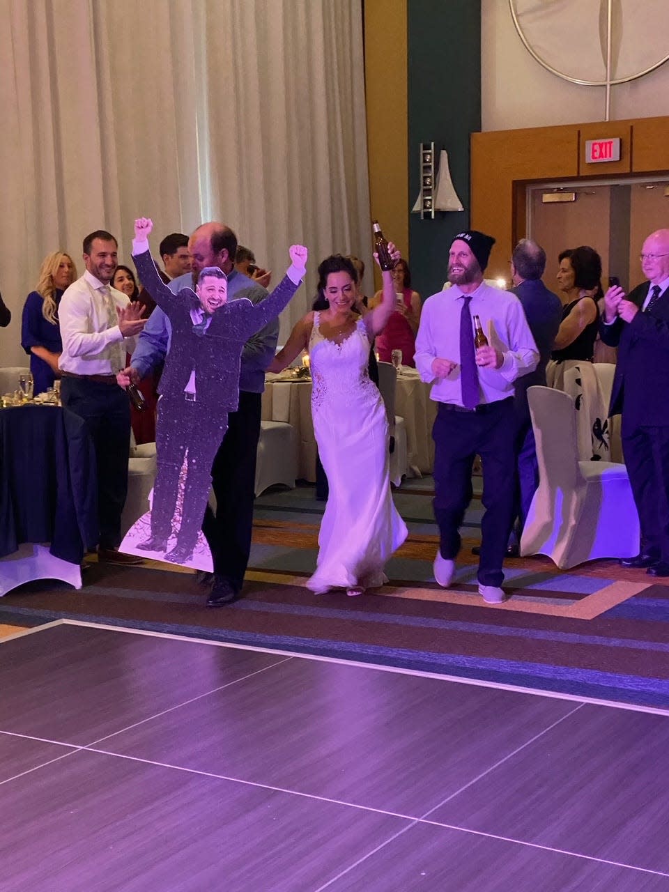 Bride enters wedding reception with cardboard cutout of the groom