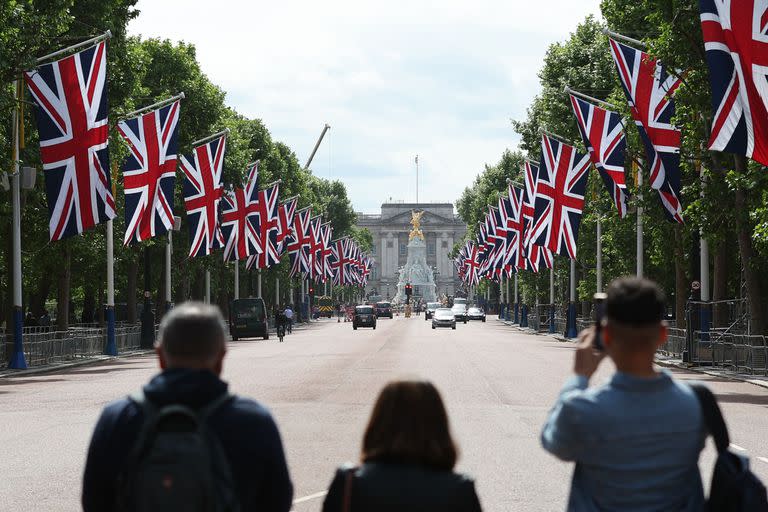 La gente toma fotografías mirando hacia el Palacio de Buckingham mientras las banderas de la Unión ondean en la brisa en preparación para el Jubileo de Platino de la Reina Isabel, en Londres, el 26 de mayo de 2022. (Photo by Adrian DENNIS / AFP)