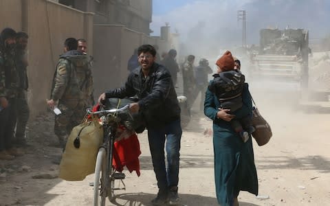 Syrians from the rebel-held Eastern Ghouta region, just outside Damascus, cross a regime-controlled corridor in Hamouria  - Credit: AFP/Getty