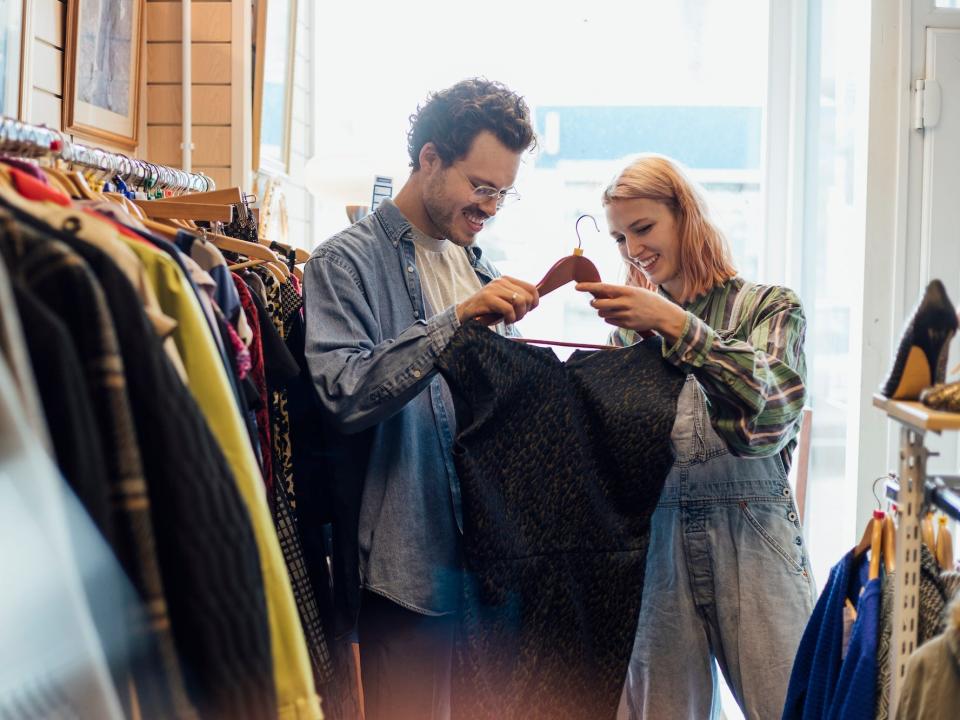 A man and a woman look at a pair of pants at a thrift store.