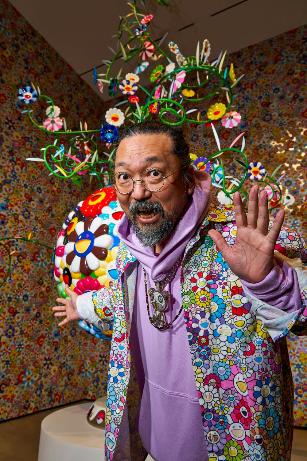 A man in colorful clothing poses in front of a art sculpture.