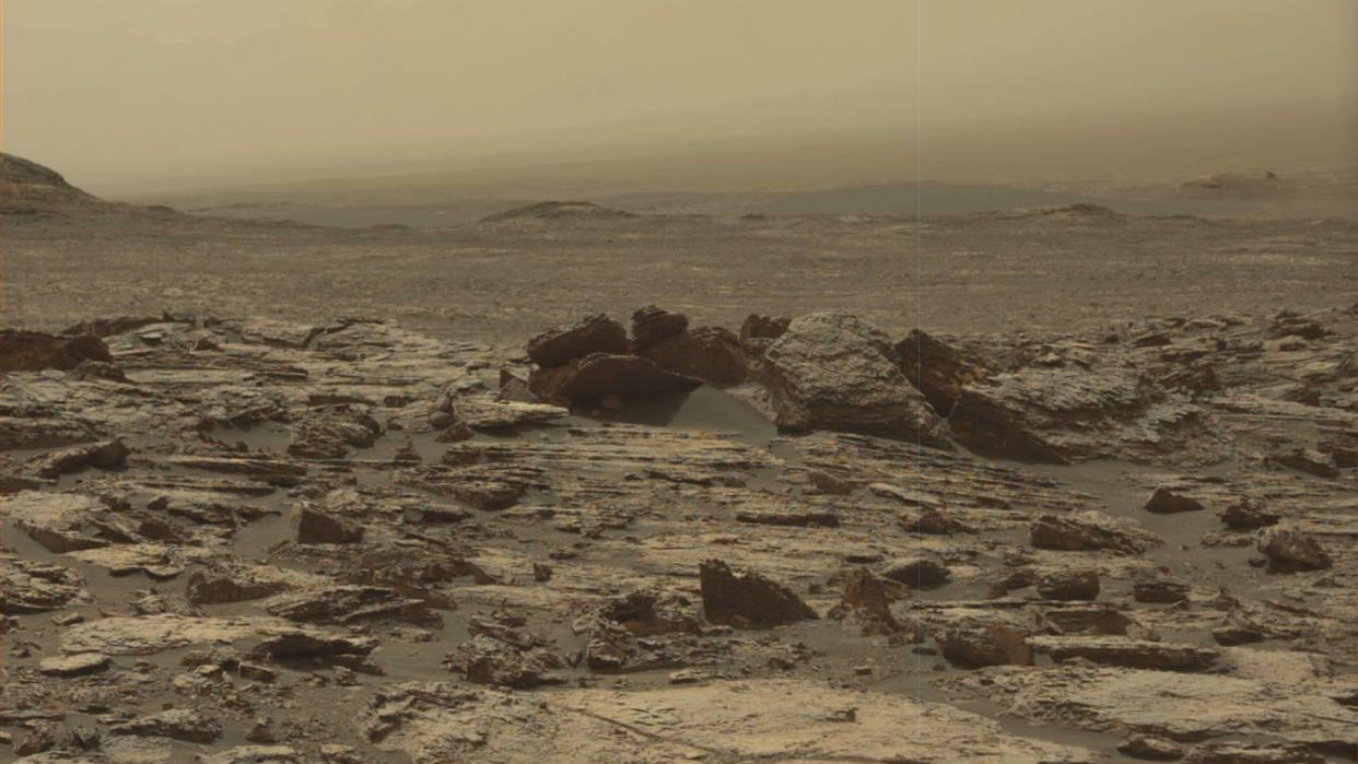  A dull yellow-tinted, rocky terrain blown with dust, as the sky in the distance matches the ground's dusty tones. 